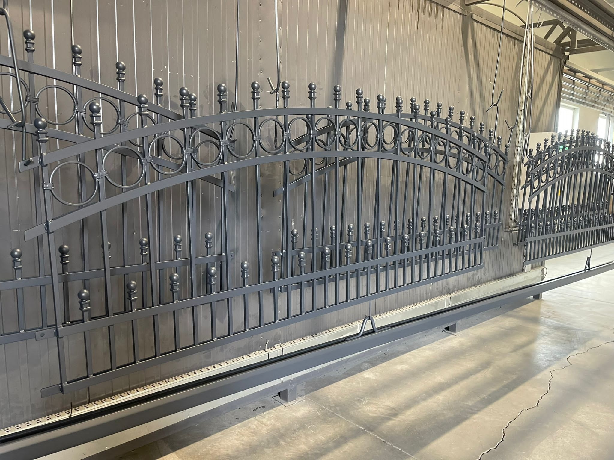 Szara, metalowa brama przesuwna z dekoracyjnymi elementami w kształcie kółek, w trakcie produkcji w Witnicy, widoczne szyny jezdne.