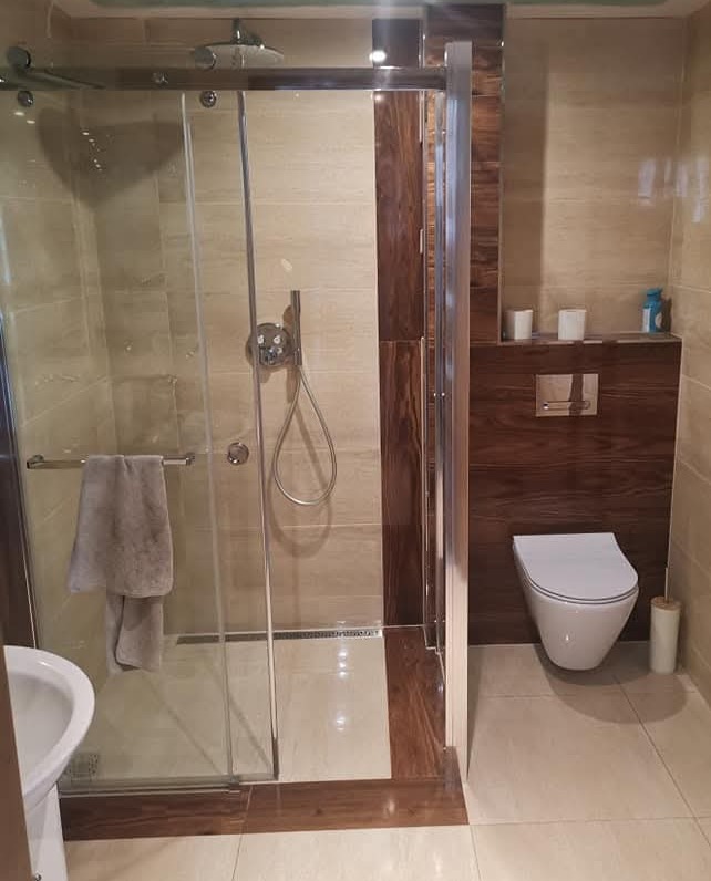 Nowoczesna łazienka z kabiną prysznicową ze szklanymi drzwiami, beżowymi płytkami i elementami z ciemnego drewna.