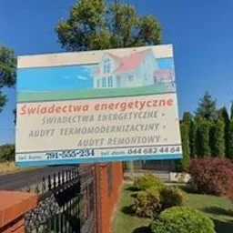 Tablica reklamowa z informacją o usługach: świadectwa energetyczne, audyt termomodernizacyjny, audyt remontowy, z ilustracją domu z czerwonym dachem, umieszczona na ogrodzeniu z cegły klinkierowej.
