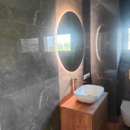 SZKŁO & ALU - Nowoczesna łazienka z umywalką nablatową, okrągłym lustrem z podświetleniem LED i marmurowymi płytkami na ścianach.