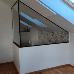 SZKŁO & ALU - Szklana ścianka działowa z czarną ramą oddzielająca przestrzeń poddasza z oknem dachowym i tapetą w kwiaty, widok na drewnianą podłogę.