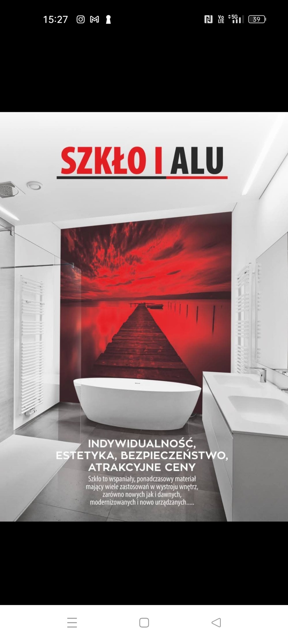 Aranżacja łazienki z panelem szklanym z motywem czerwonego zachodu słońca nad jeziorem i pomostem, biała wanna wolnostojąca i umywalka w zabudowie, grzejnik drabinkowy.