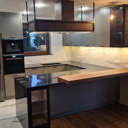 BEGI sp. z o.o. - Nowoczesna kuchnia z szarymi szafkami, marmurowym blatem i drewnianymi akcentami. Wyspa z czarnym blatem i drewnianym barkiem. Oświetlenie LED pod szafkami.