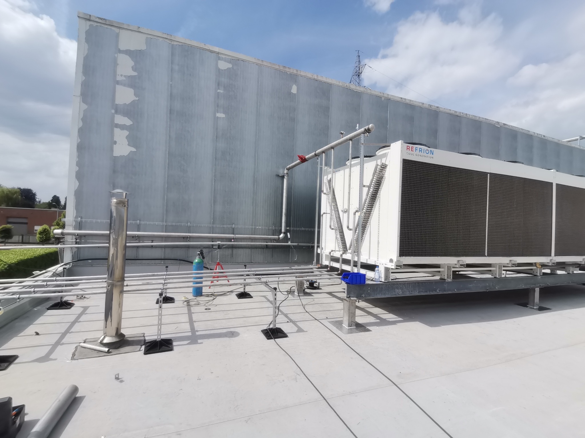 Instalacja chłodnicza REFRION na dachu budynku przemysłowego, widoczne rurociągi, butla z gazem technicznym i elementy konstrukcji stalowej.