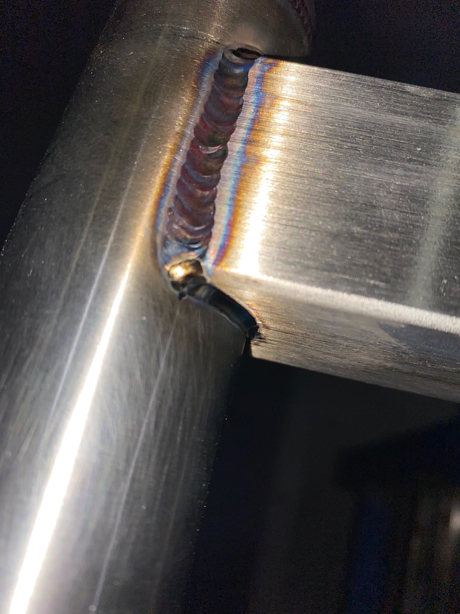 Szczegółowe zbliżenie na spawany, nierdzewny narożnik. Widoczne tęczowe przebarwienia po spawaniu i precyzyjne wykonanie spoiny na metalowej konstrukcji.