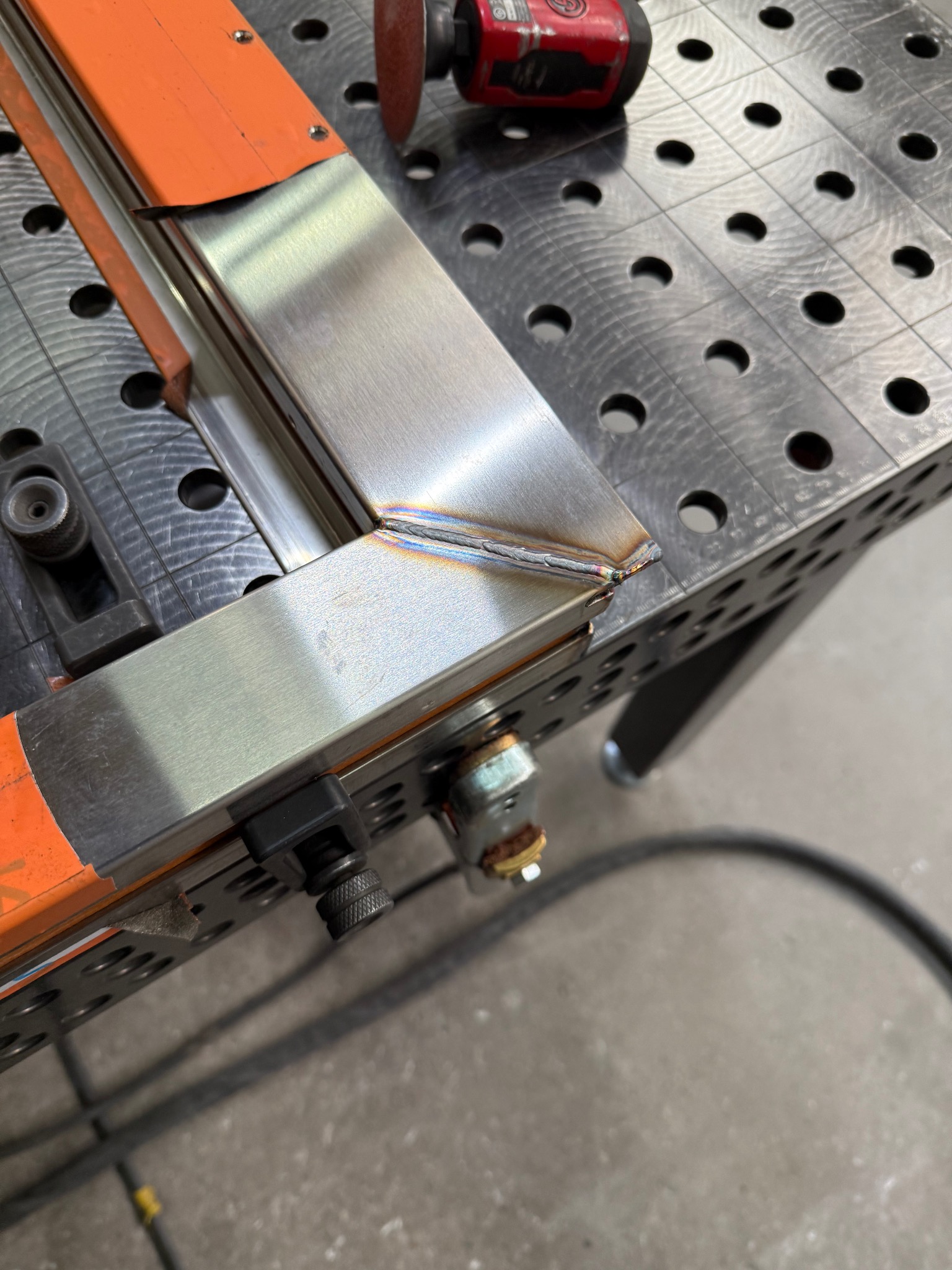 Spoina narożna na metalowym profilu, wykonana w Gdańsku. Widoczny stół spawalniczy z otworami i narzędzie szlifierskie.