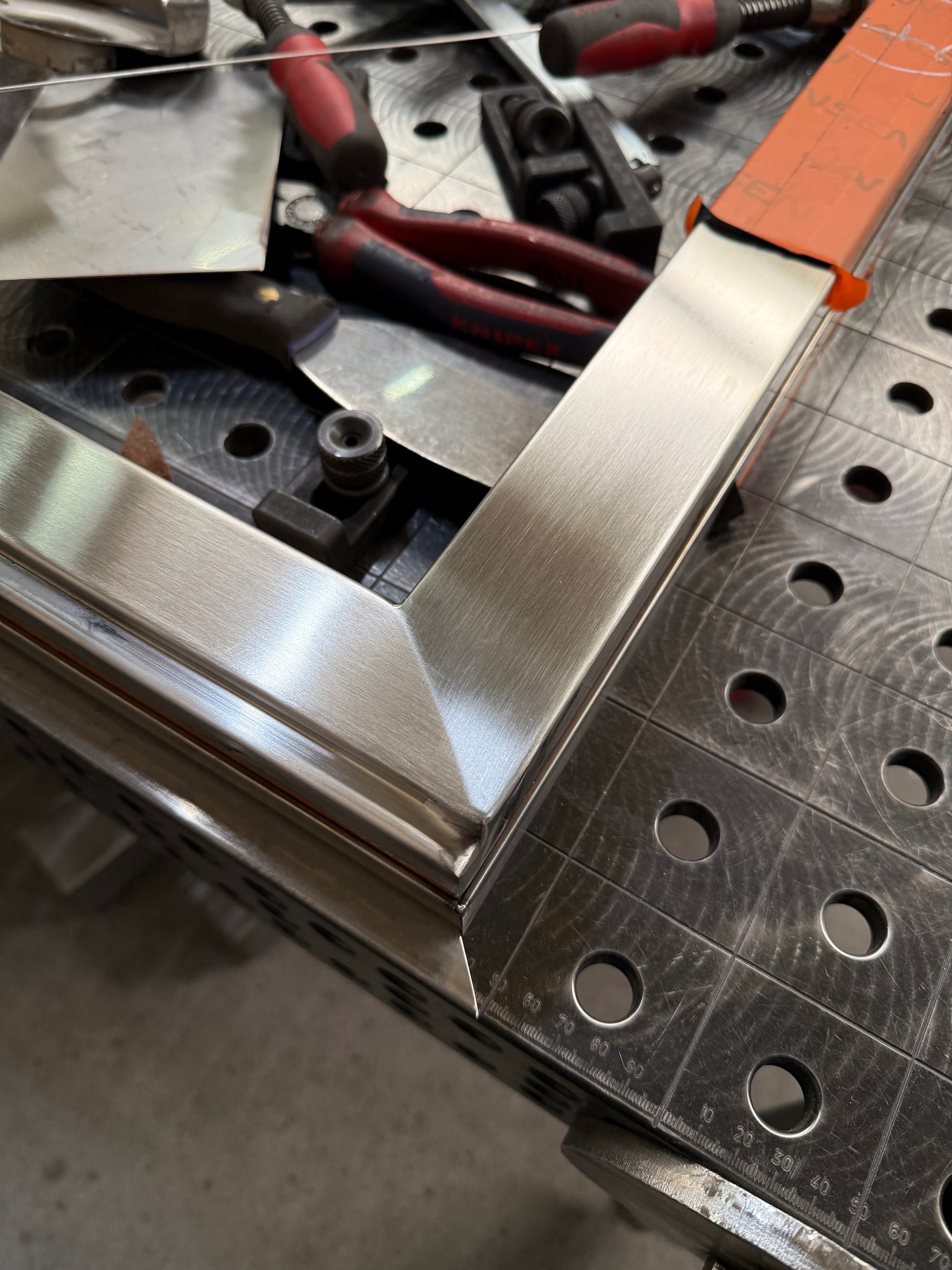 Nierdzewny narożnik ramy na stole spawalniczym z narzędziami. Precyzyjne połączenie elementów, widoczne detale szlifowania i wykończenia.