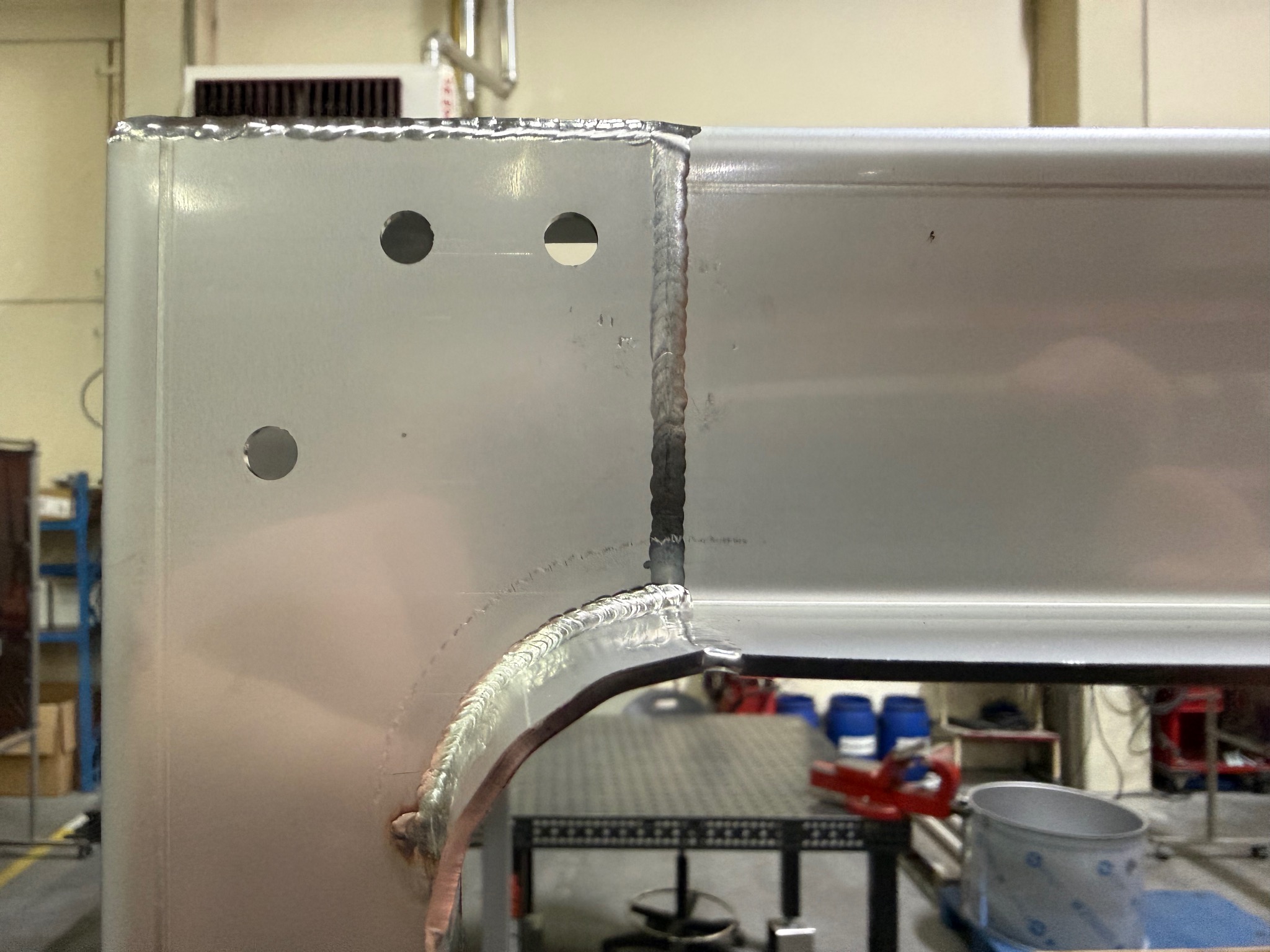 Szlifowany metalowy element konstrukcyjny z otworami i widocznymi spawami, ukazujący precyzję wykonania i solidność połączeń. Detal w warsztacie.