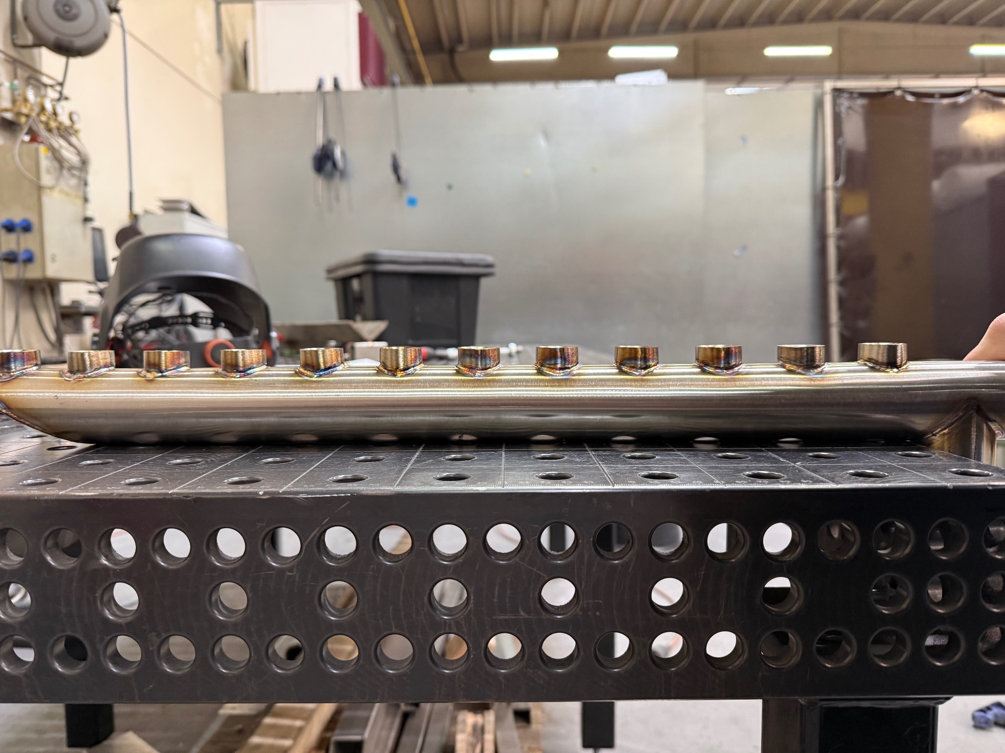 Spawana rura ze stali nierdzewnej z precyzyjnymi spawami, leżąca na perforowanym stole spawalniczym w warsztacie. Widoczne ślady ciepła na spawach.