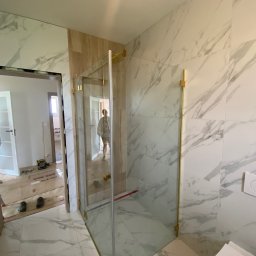 ART-FLIZ - Nowoczesna kabina prysznicowa ze złotymi okuciami i marmurowymi płytkami w trakcie montażu, widoczne narzędzia i osoba w tle.