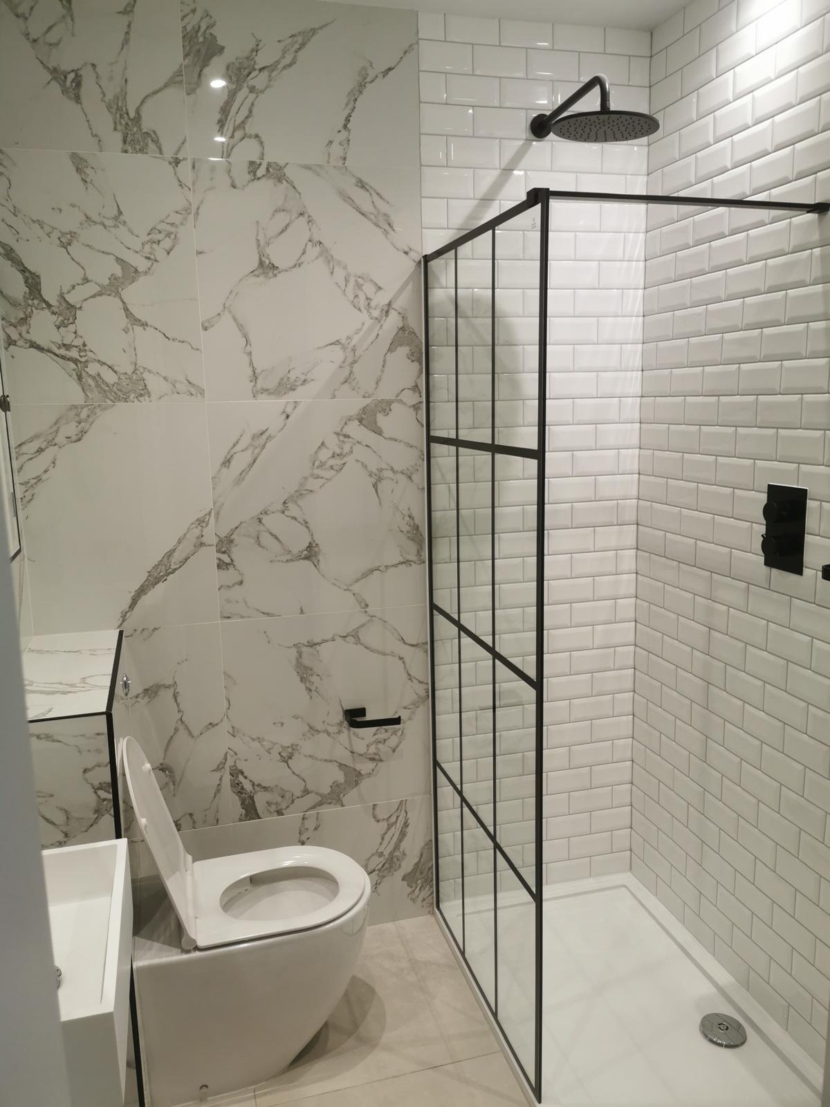 Nowoczesna łazienka z kabiną prysznicową typu walk-in z czarnymi profilami, płytkami imitującymi marmur na ścianie i białą ceramiką sanitarną.