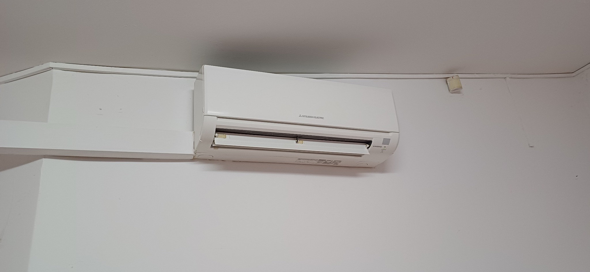 Biała klimatyzacja Mitsubishi Electric na ścianie, z otwartą klapką wylotu powietrza. Widoczne detale montażu i czysta powierzchnia urządzenia.