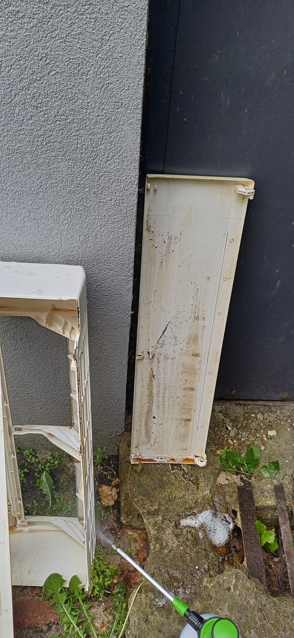 Czyszczenie zabrudzonych elementów klimatyzacji myjką ciśnieniową na zewnątrz budynku. Widoczne fragmenty obudowy i osłony.