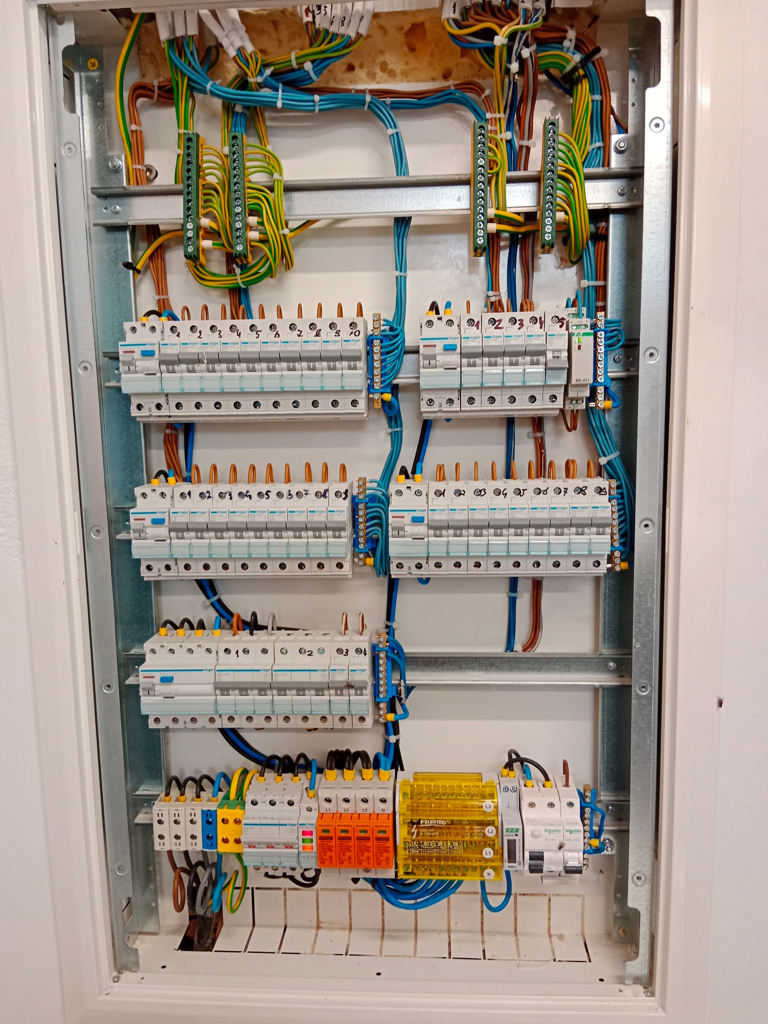 Rozdzielnia elektryczna z zainstalowanymi bezpiecznikami, przewodami o różnych kolorach i listwami zaciskowymi, widoczne oznaczenia na bezpiecznikach i elementach rozdzielnicy.