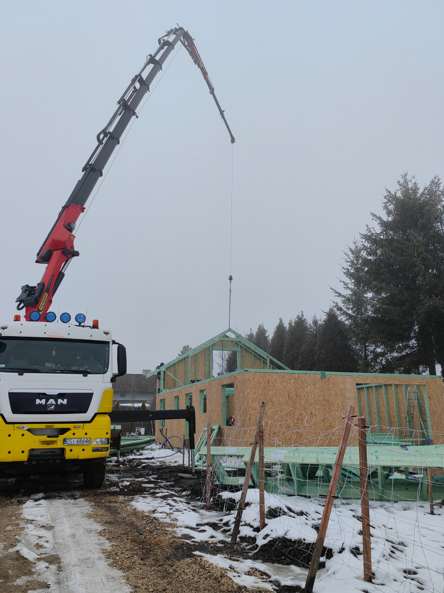 Montaż konstrukcji domu z wykorzystaniem dźwigu MAN na placu budowy w zimowy dzień.