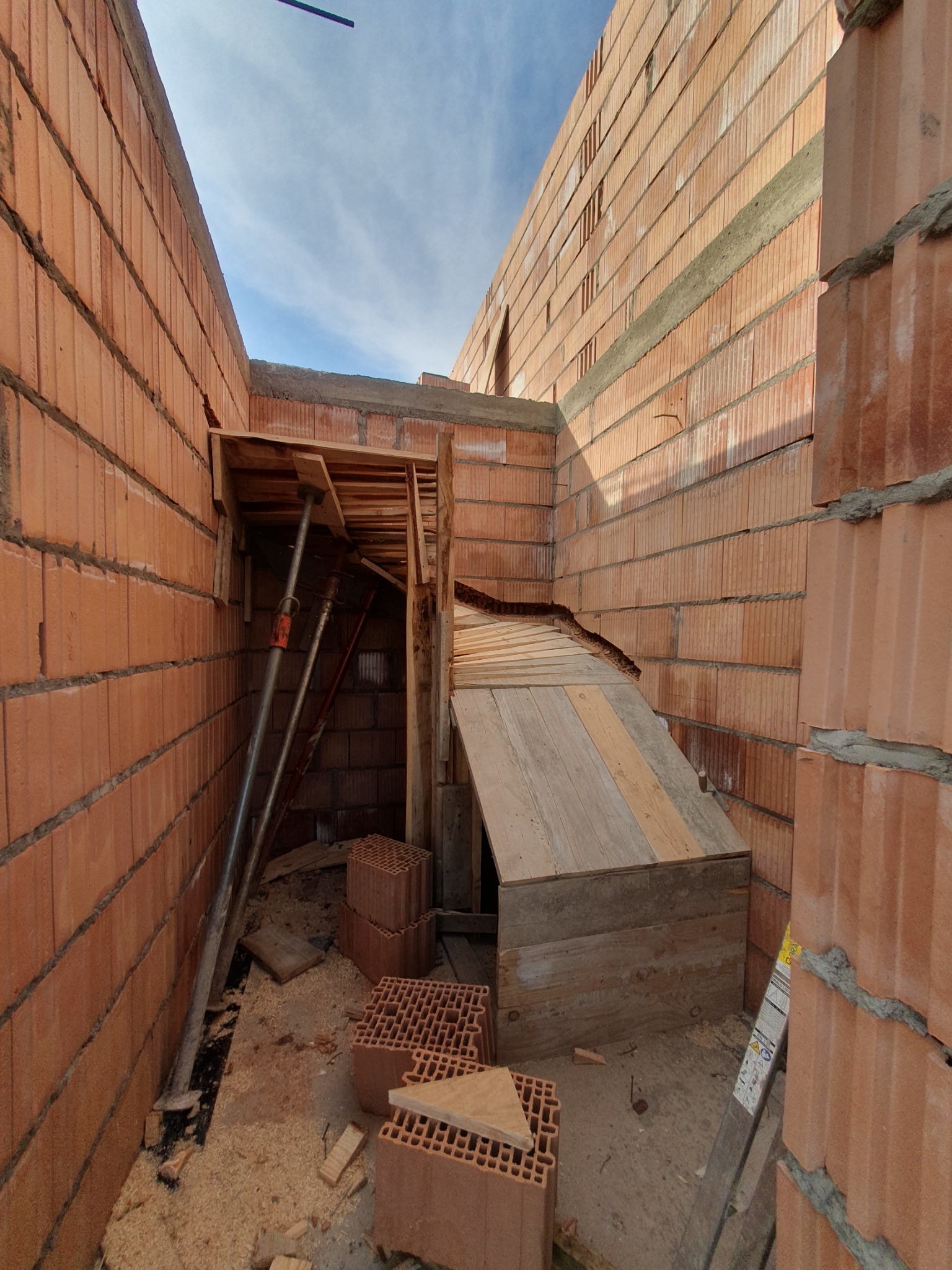 Wnętrze budowanego domu z cegły ceramicznej, widoczne podpory stropu i drewniane szalunki, porozrzucane trociny na podłodze.