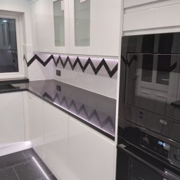 Krzysztof Sitniewski - Nowoczesna, czarno-biała kuchnia z błyszczącym, czarnym blatem i podświetleniem LED, wzór zygzak na ścianie, zabudowany piekarnik AEG.