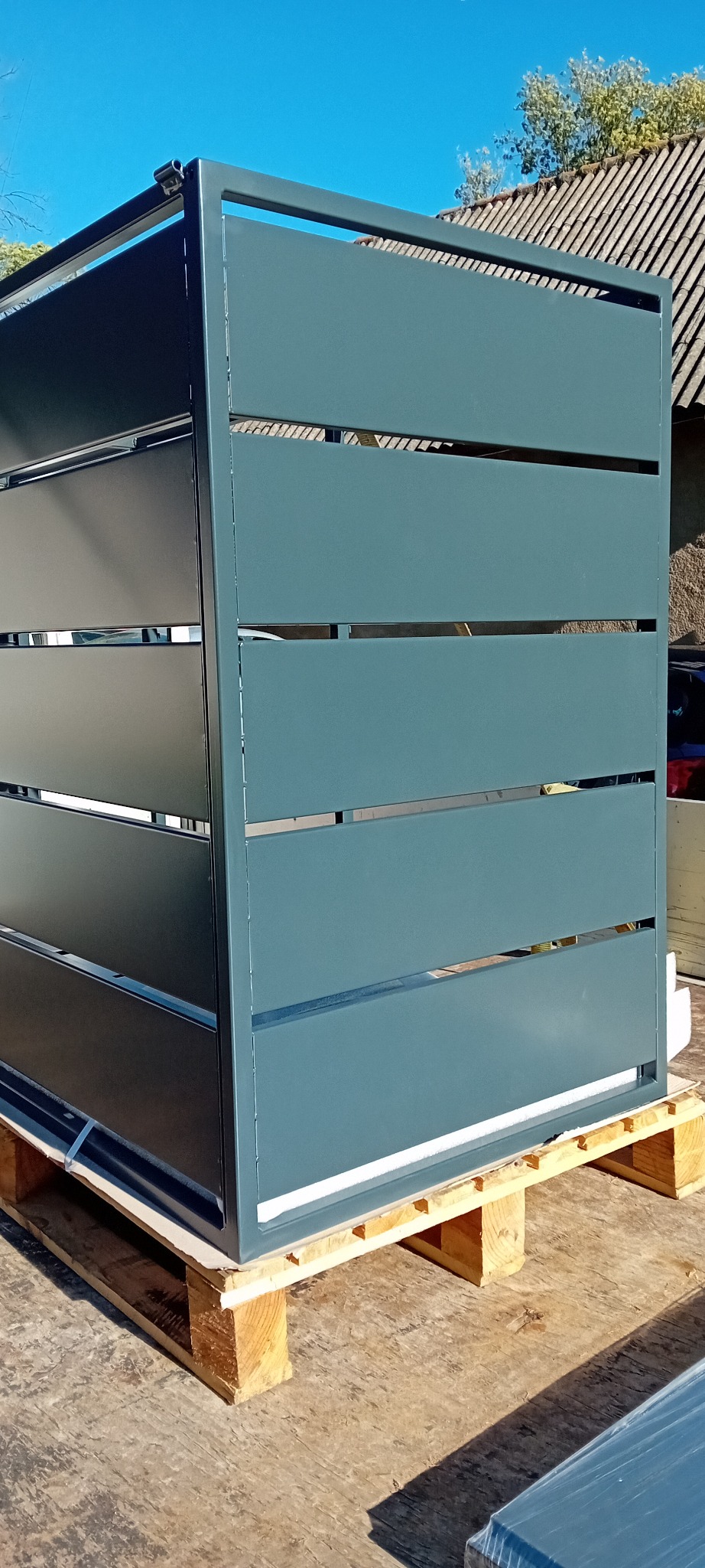 Gotowa, pomalowana na szaro, metalowa konstrukcja z poziomymi szczelinami, umieszczona na drewnianej palecie, przygotowana do transportu.