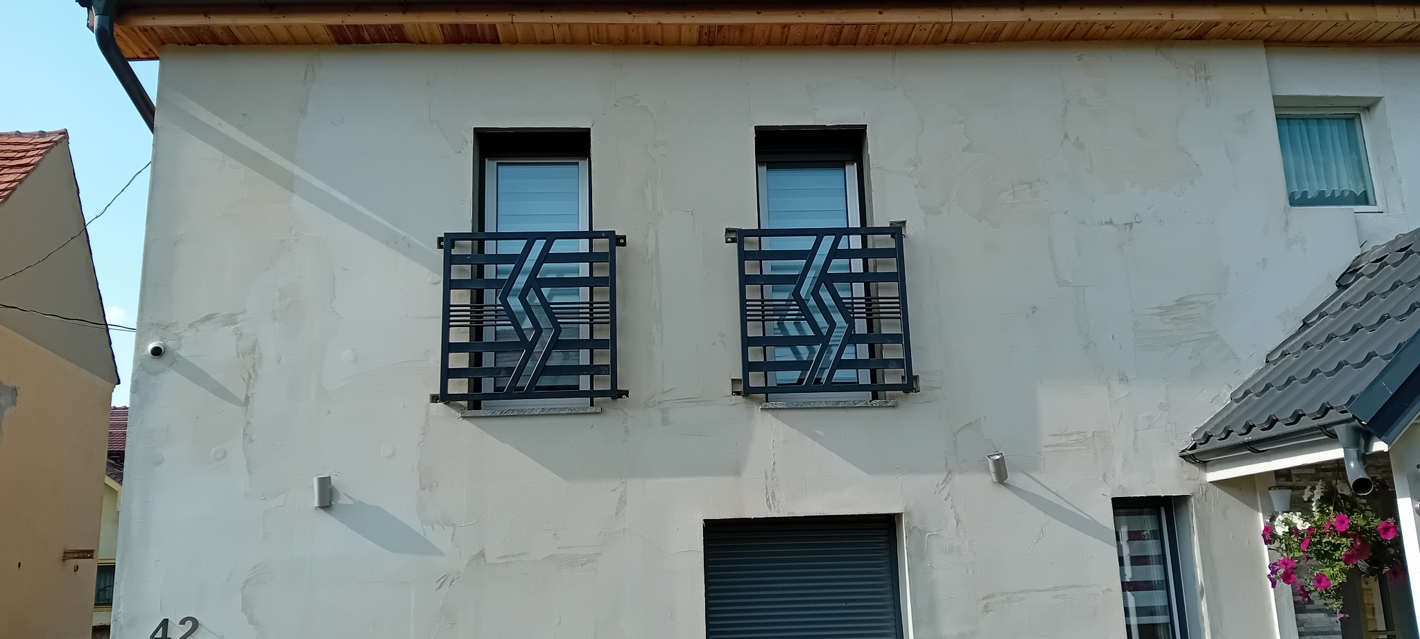 Dwa okna na elewacji budynku z czarnymi, metalowymi balustradami o geometrycznym wzorze, widok z zewnątrz.