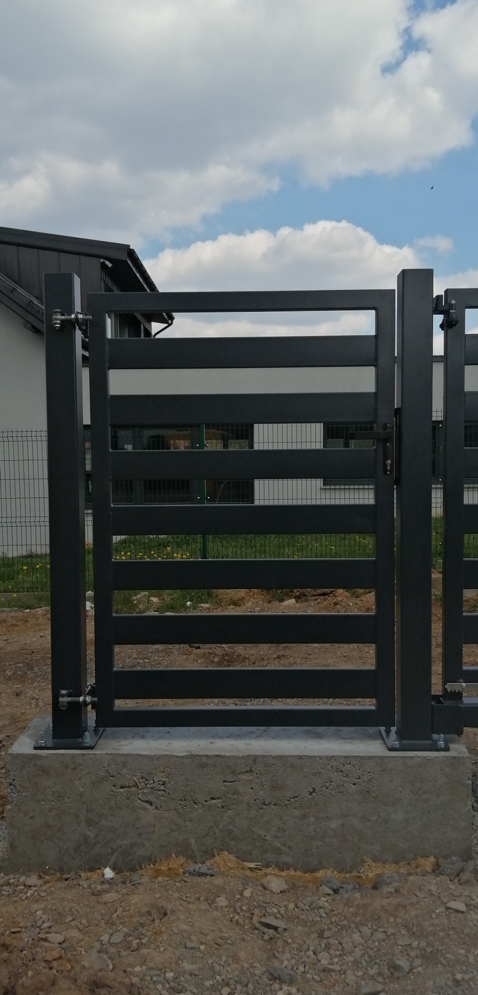 Nowoczesna, pozioma brama wjazdowa z metalu, pomalowana na ciemny kolor, zamontowana na betonowej podstawie, z widocznym ogrodzeniem panelowym w tle.
