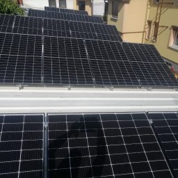 EkoOszczędni - Panele fotowoltaiczne zamontowane na białym dachu budynku mieszkalnego, widoczne okna i drabina na elewacji.