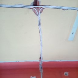 Kamil Duda - Białe przewody elektryczne prowadzone w bruzdach w ścianie i suficie, widoczne fragmenty cegły w miejscu łączenia przewodów.