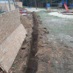 Kamil Duda - Wkopany przewód w ziemi, widoczny wykop w pobliżu placu zabaw, zabezpieczony płytami OSB.