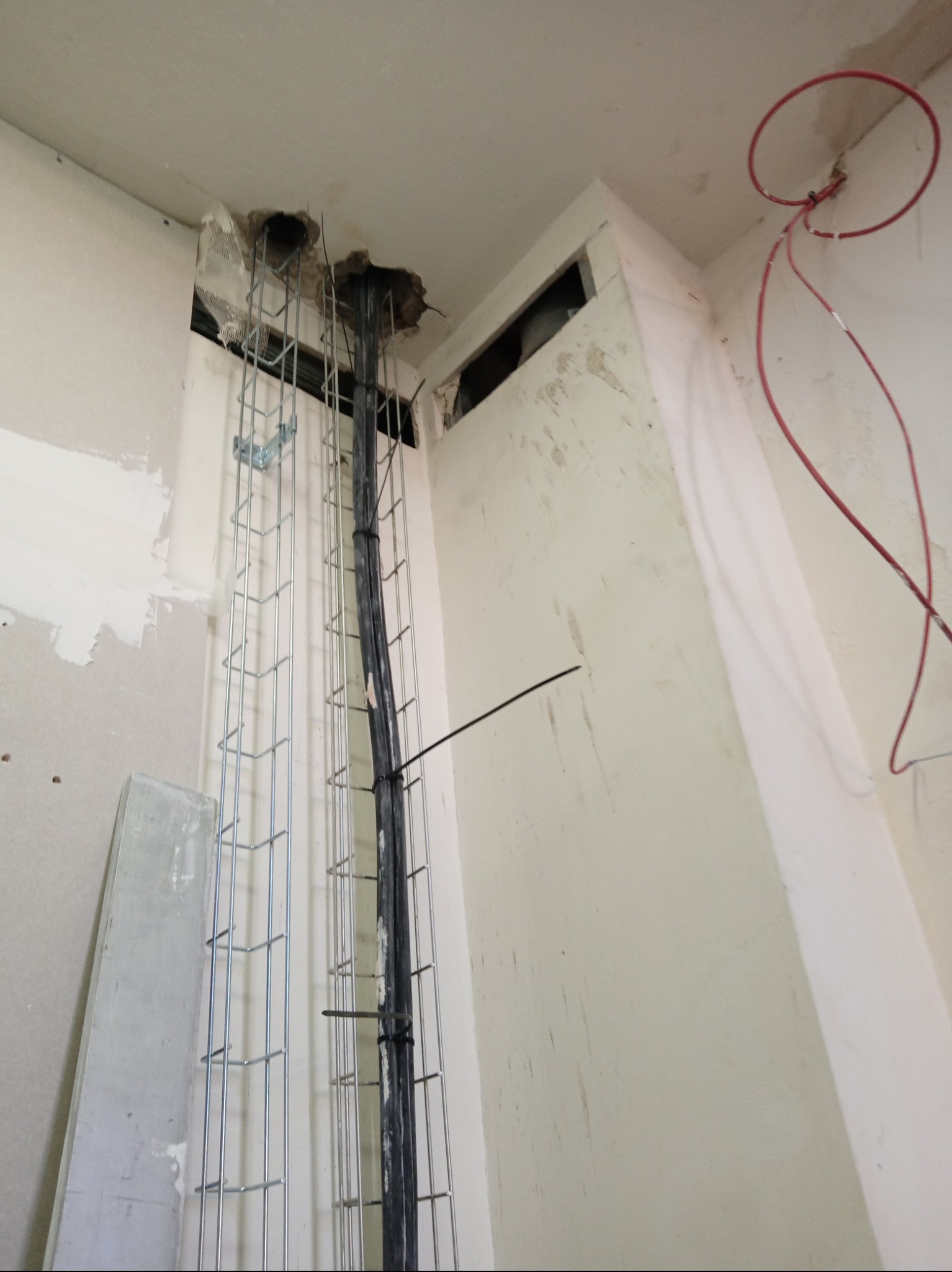 Wewnętrzna instalacja elektryczna w trakcie montażu: widoczne przewody w korytku mocowanym do ściany, otwory w suficie i fragmenty niezakończonej zabudowy z płyt gipsowo-kartonowych.