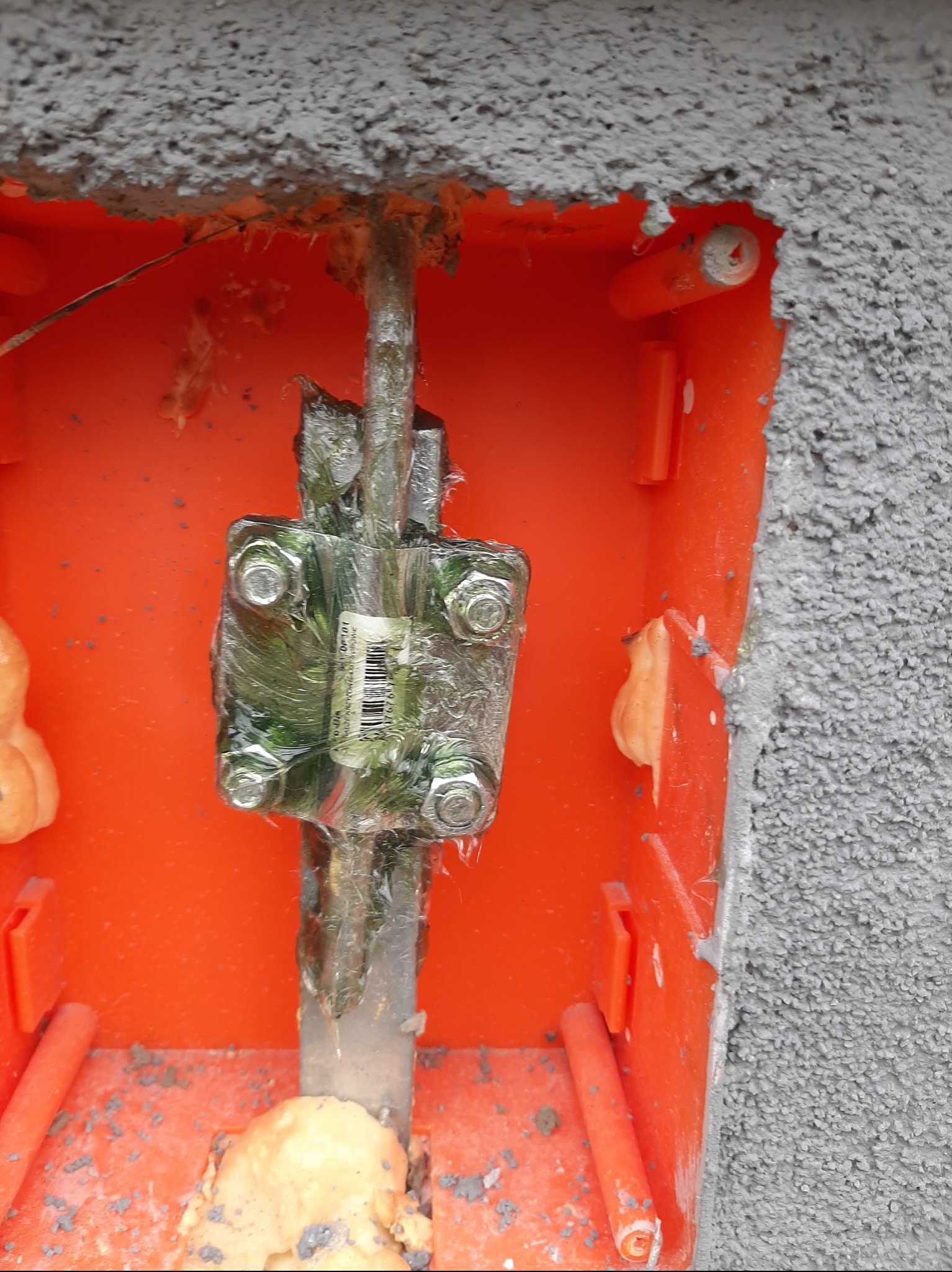 Uziemienie instalacji odgromowej w pomarańczowej puszce, zabezpieczone folią, widoczne ślady pianki montażowej.