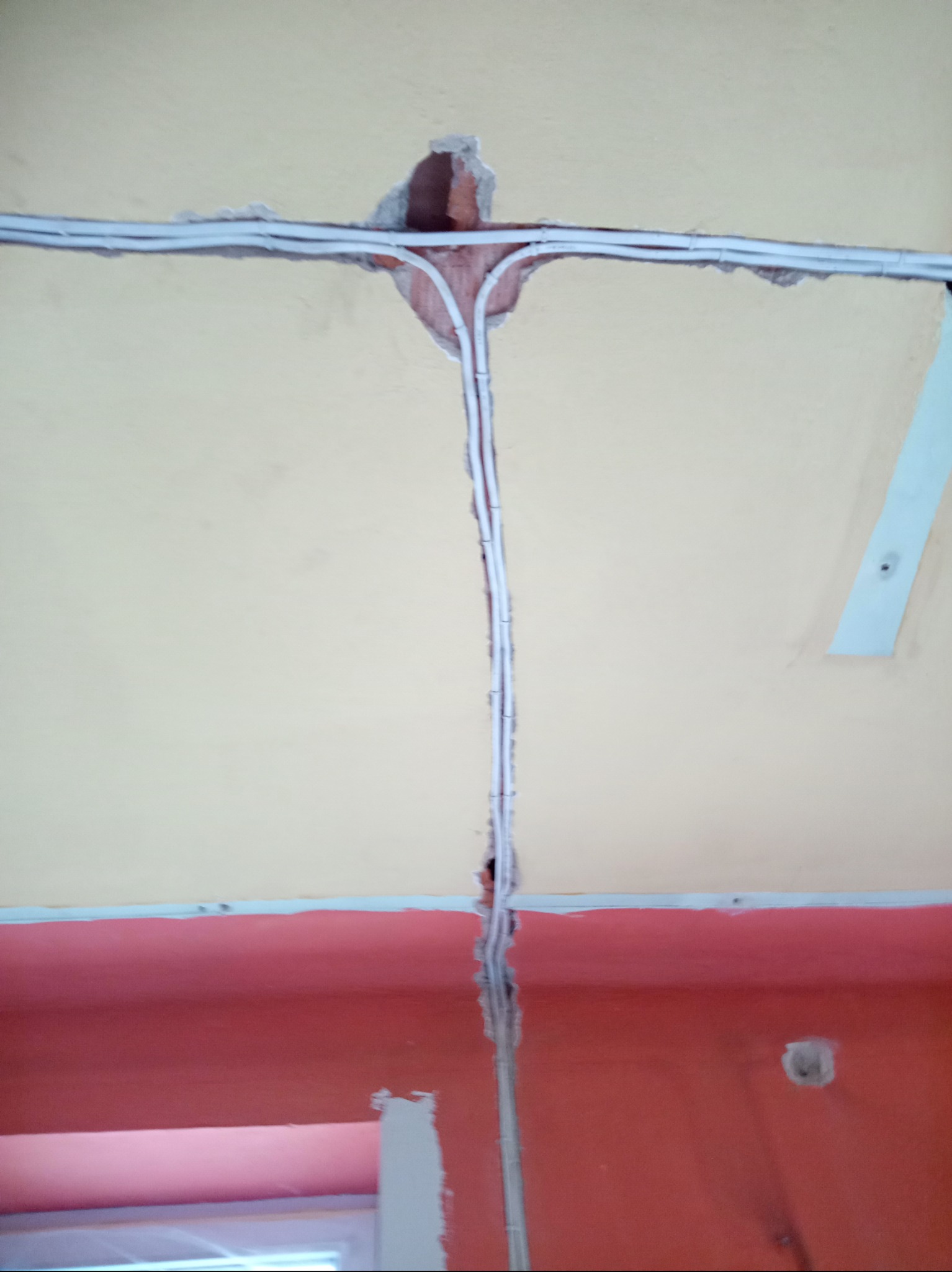 Białe przewody elektryczne prowadzone w bruzdach w ścianie i suficie, widoczne fragmenty cegły w miejscu łączenia przewodów.