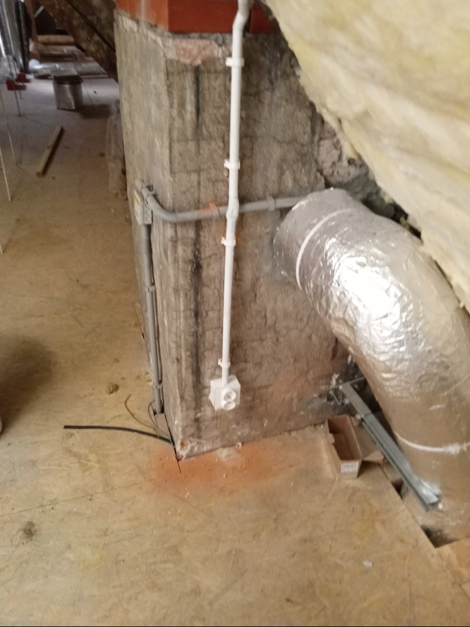 Instalacja elektryczna w surowym wnętrzu poddasza: białe rury z puszkami, szara rura karbowana, fragment izolacji termicznej pokrytej folią aluminiową, widok na podłogę z płyty OSB.
