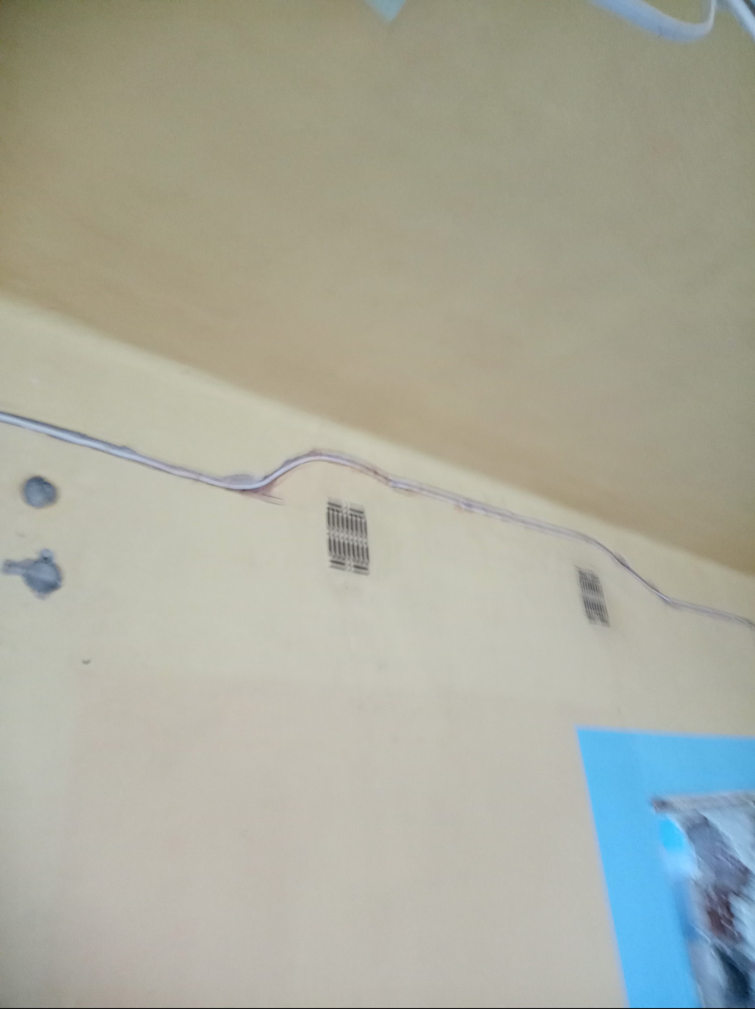 Kabel elektryczny prowadzony po ścianie wewnątrz pomieszczenia, widoczne puszki instalacyjne i kratka wentylacyjna.