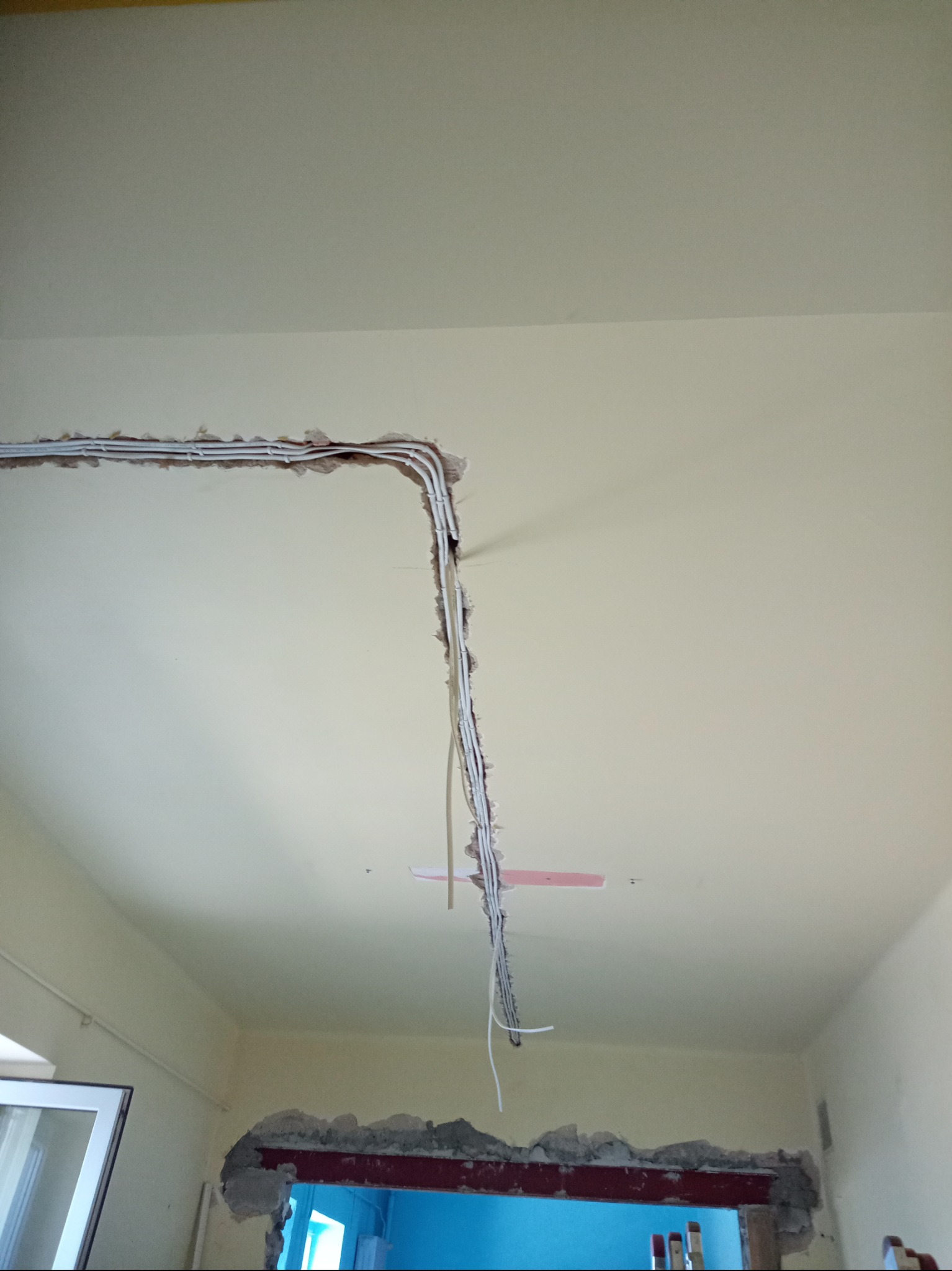 Białe przewody elektryczne ułożone w bruździe pod sufitem w trakcie remontu pomieszczenia, widoczne fragmenty gruzu i farby.