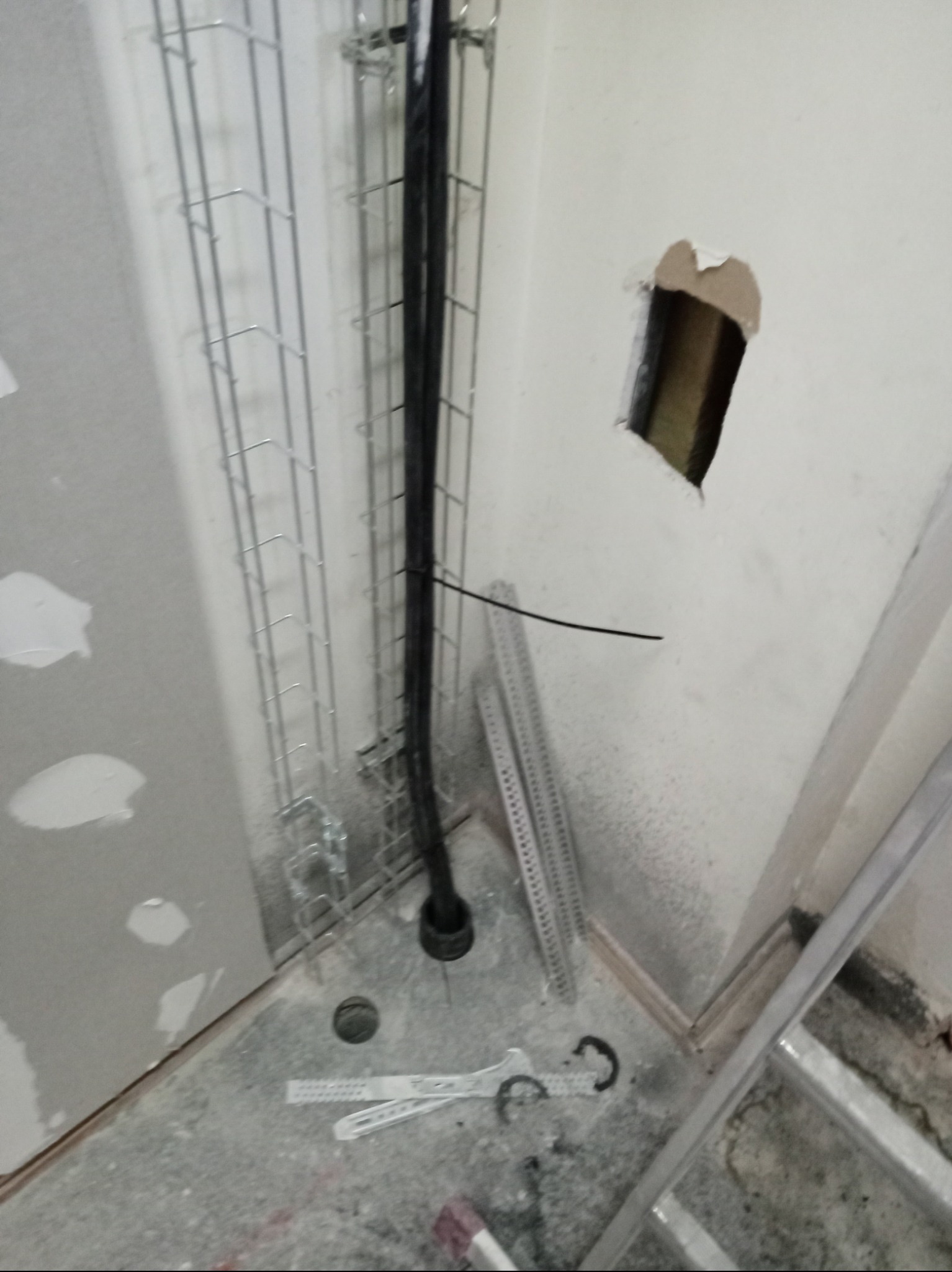 Przewody elektryczne prowadzone w korycie kablowym, widoczne elementy instalacji w surowym stanie, otwór w ścianie. W tle drabina.