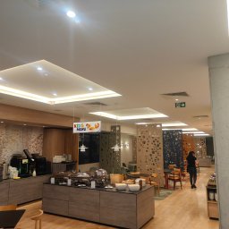 Vitalii Stefaniuk Next - Haus - Nowoczesna aranżacja wnętrza hotelowej restauracji z bufetem śniadaniowym, dekoracyjnymi panelami ażurowymi i oświetleniem LED. Widoczny napis 'Kids Menu'.