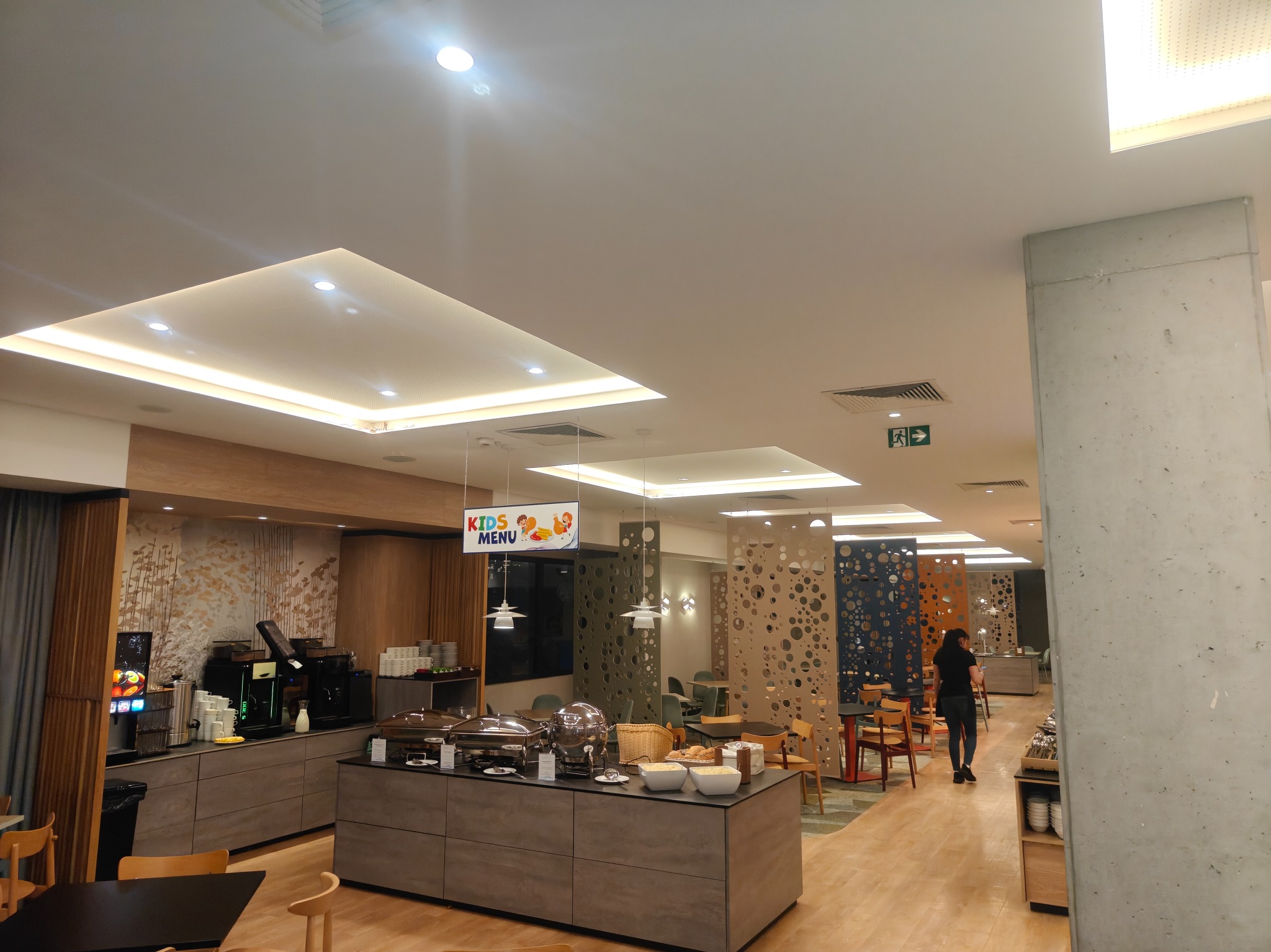 Nowoczesna aranżacja wnętrza hotelowej restauracji z bufetem śniadaniowym, dekoracyjnymi panelami ażurowymi i oświetleniem LED. Widoczny napis 'Kids Menu'.