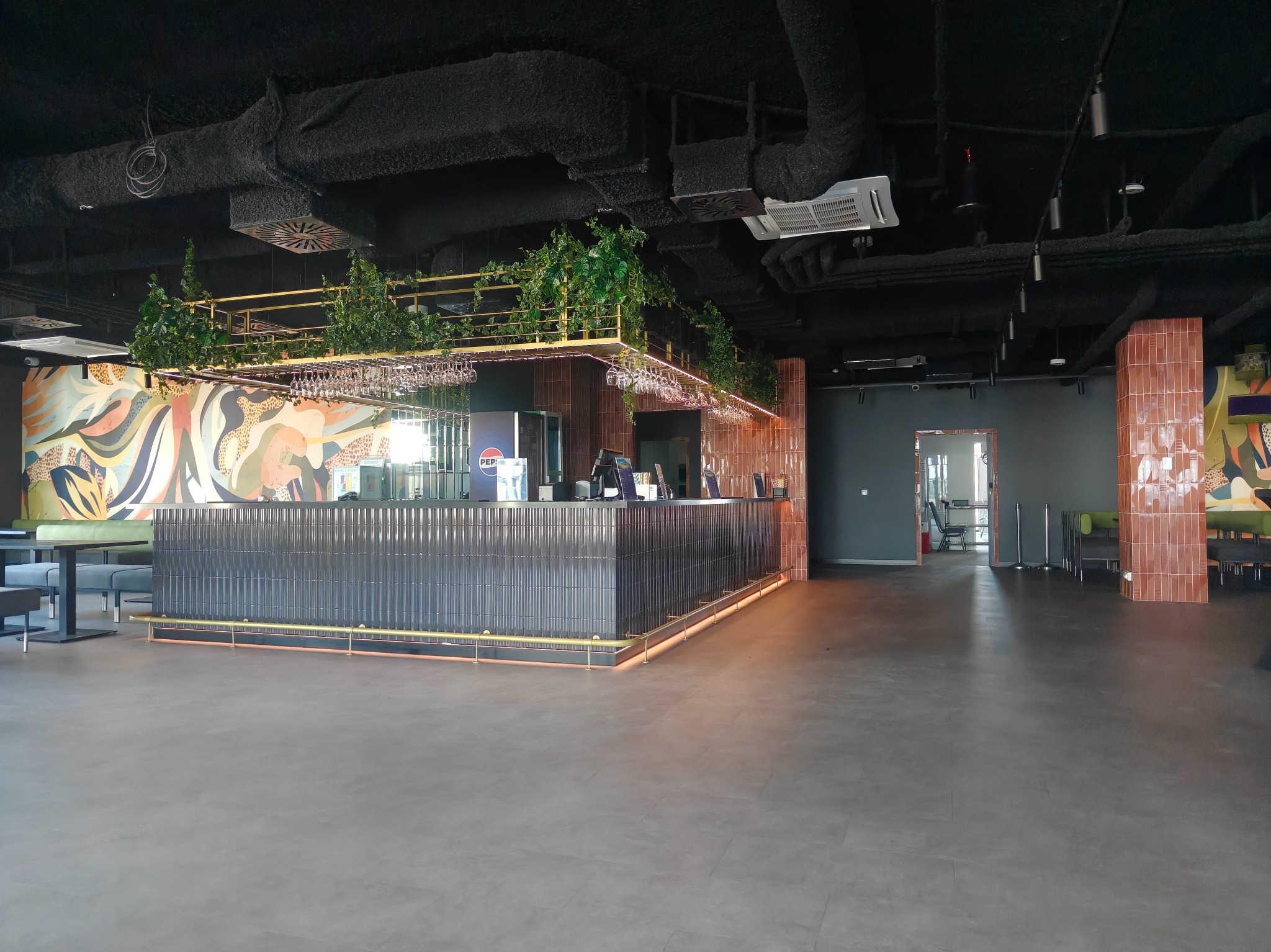 Nowoczesne wykończenie wnętrza lokalu usługowego: bar z ciemnymi płytkami, oświetleniem LED i elementami dekoracyjnymi, widok na przestronne wnętrze.