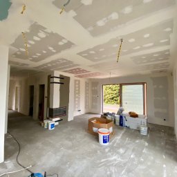 Wall Done Szymon Andrysiak - Wnętrze w trakcie remontu: ściany i sufit po szpachlowaniu, widoczne kable zwisające z sufitu, przygotowane materiały budowlane i narzędzia na podłodze.