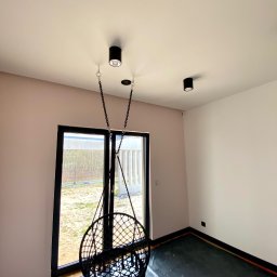 Wall Done Szymon Andrysiak - Pokój po malowaniu ścian na dwa kolory, z zamontowanym fotelem wiszącym na łańcuchu i lampami sufitowymi, podłoga zabezpieczona folią malarską.