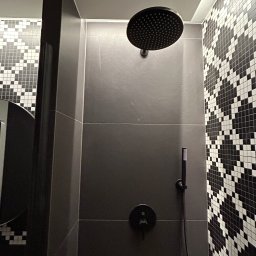 Wall Done Szymon Andrysiak - Nowoczesna kabina prysznicowa z czarną armaturą i grafitowymi płytkami, akcentowana mozaiką w biało-czarną szachownicę.