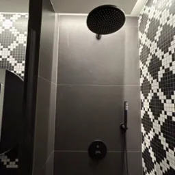 Nowoczesna kabina prysznicowa z czarną armaturą i grafitowymi płytkami, akcentowana mozaiką w biało-czarną szachownicę.