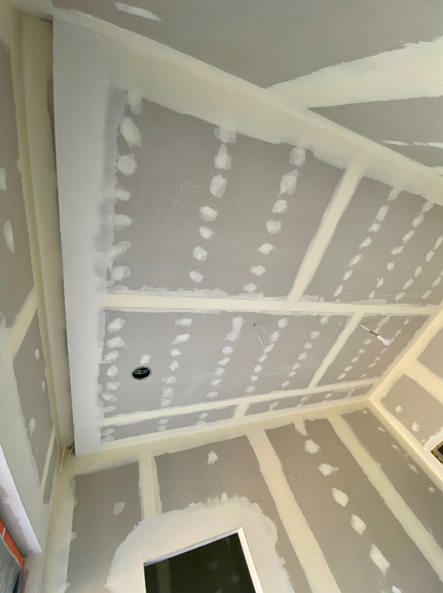 Sufit i ściany z płyt kartonowo-gipsowych, z widocznymi łączeniami i miejscami po wkrętach wypełnionymi masą szpachlową, przygotowane do dalszego etapu prac wykończeniowych.