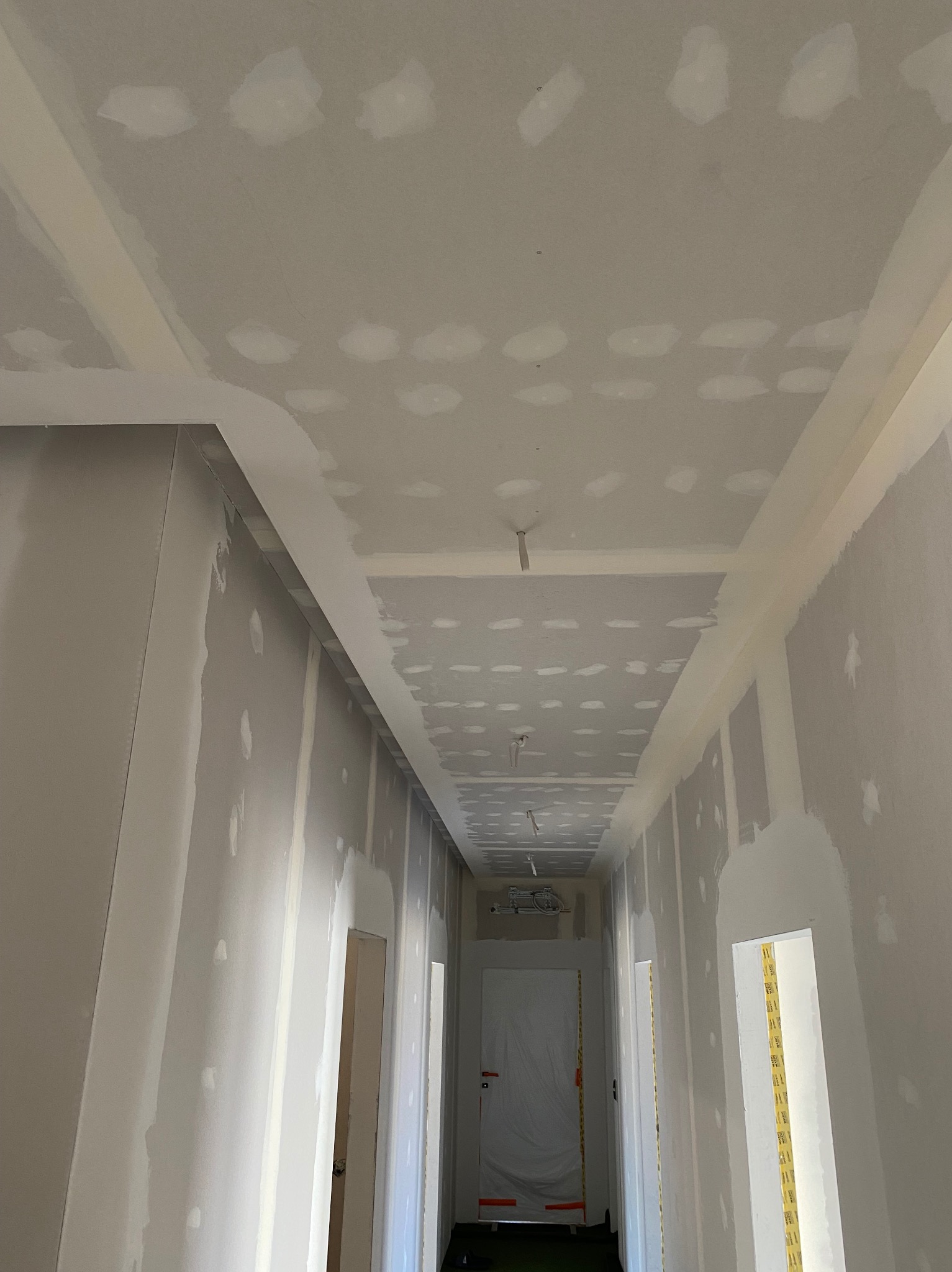 Korytarz w trakcie prac wykończeniowych, ściany i sufit pokryte warstwą szpachli z widocznymi punktowymi poprawkami, przygotowane do dalszego etapu.