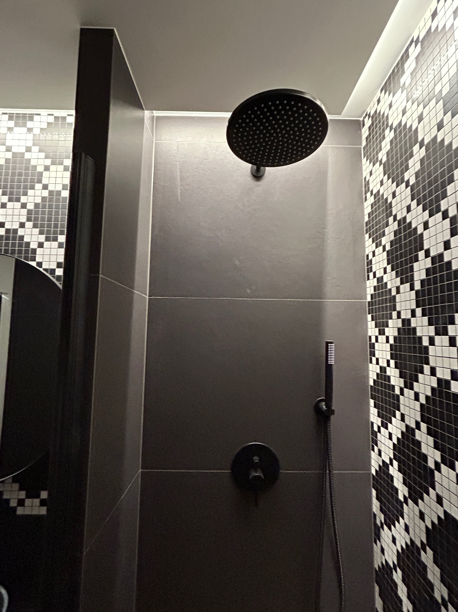 Nowoczesna kabina prysznicowa z czarną armaturą i grafitowymi płytkami, akcentowana mozaiką w biało-czarną szachownicę.