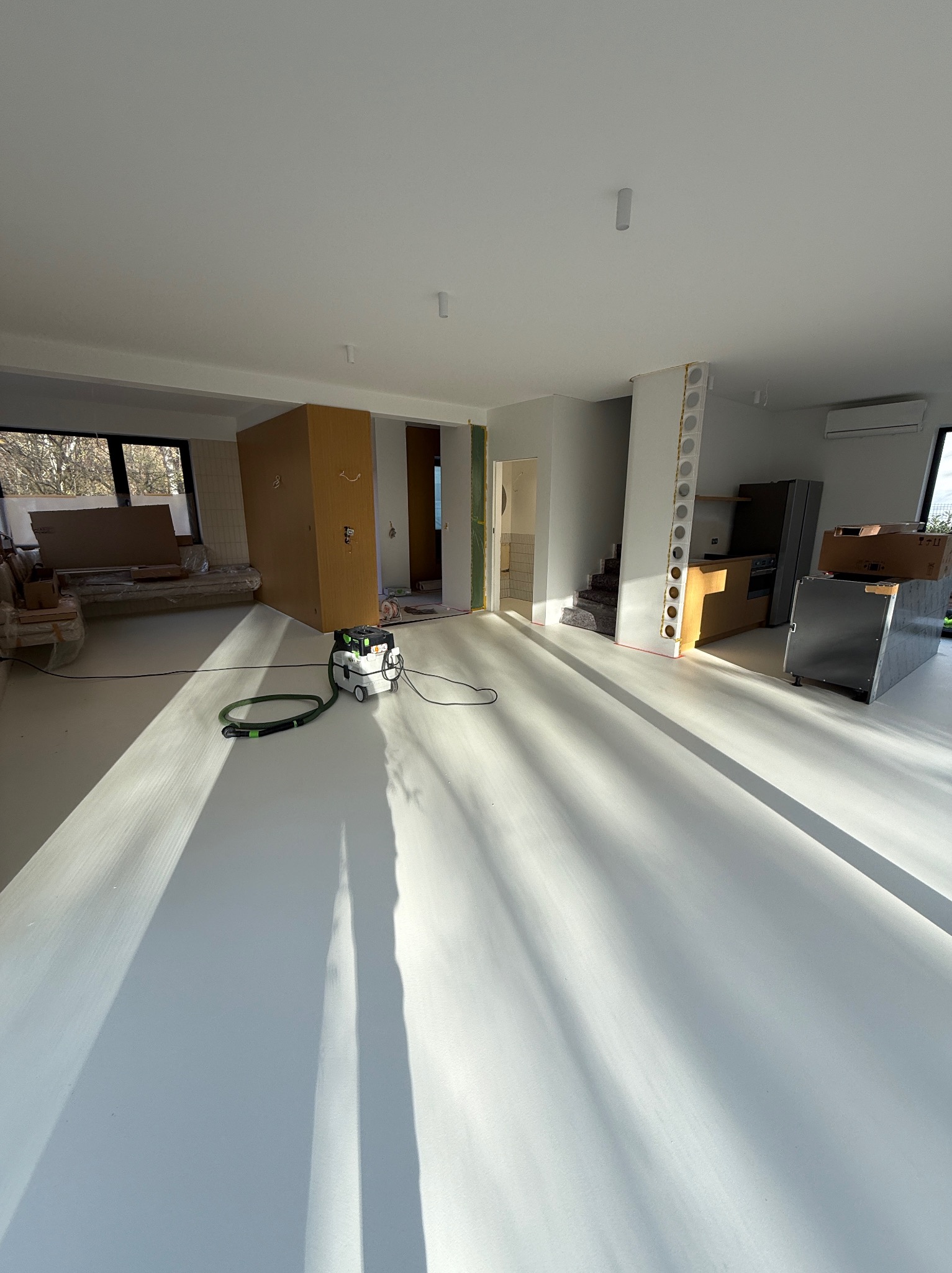 Biała, świeżo wylana posadzka w przestronnym wnętrzu w Zduńskiej Woli, z widocznym odkurzaczem przemysłowym i elementami przygotowanymi do dalszych prac wykończeniowych.