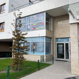 PARTNER TEMPS SPÓŁKA Z OGRANICZONĄ ODPOWIEDZIALNOŚCIĄ - Fasada budynku agencji rekrutacyjnej Partner Temps z widocznymi oknami z ofertami pracy i legalizacji pobytu dla obcokrajowców, drzewko przed wejściem.