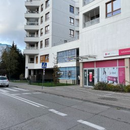 PARTNER TEMPS SPÓŁKA Z OGRANICZONĄ ODPOWIEDZIALNOŚCIĄ - Budynek z biurami usług dla firm, w tym kadry i legalizacja pobytu, widoczny z ulicy z przejściem dla pieszych i zaparkowanym samochodem.