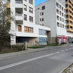 PARTNER TEMPS SPÓŁKA Z OGRANICZONĄ ODPOWIEDZIALNOŚCIĄ - Fasada budynku z biurami usługowych firm, w tym 'Kadry Place' z widocznym logo i danymi kontaktowymi, oraz 'Centrum Legalizacji' z flagami i mapą świata na szybie, widziana z perspektywy ulicy.