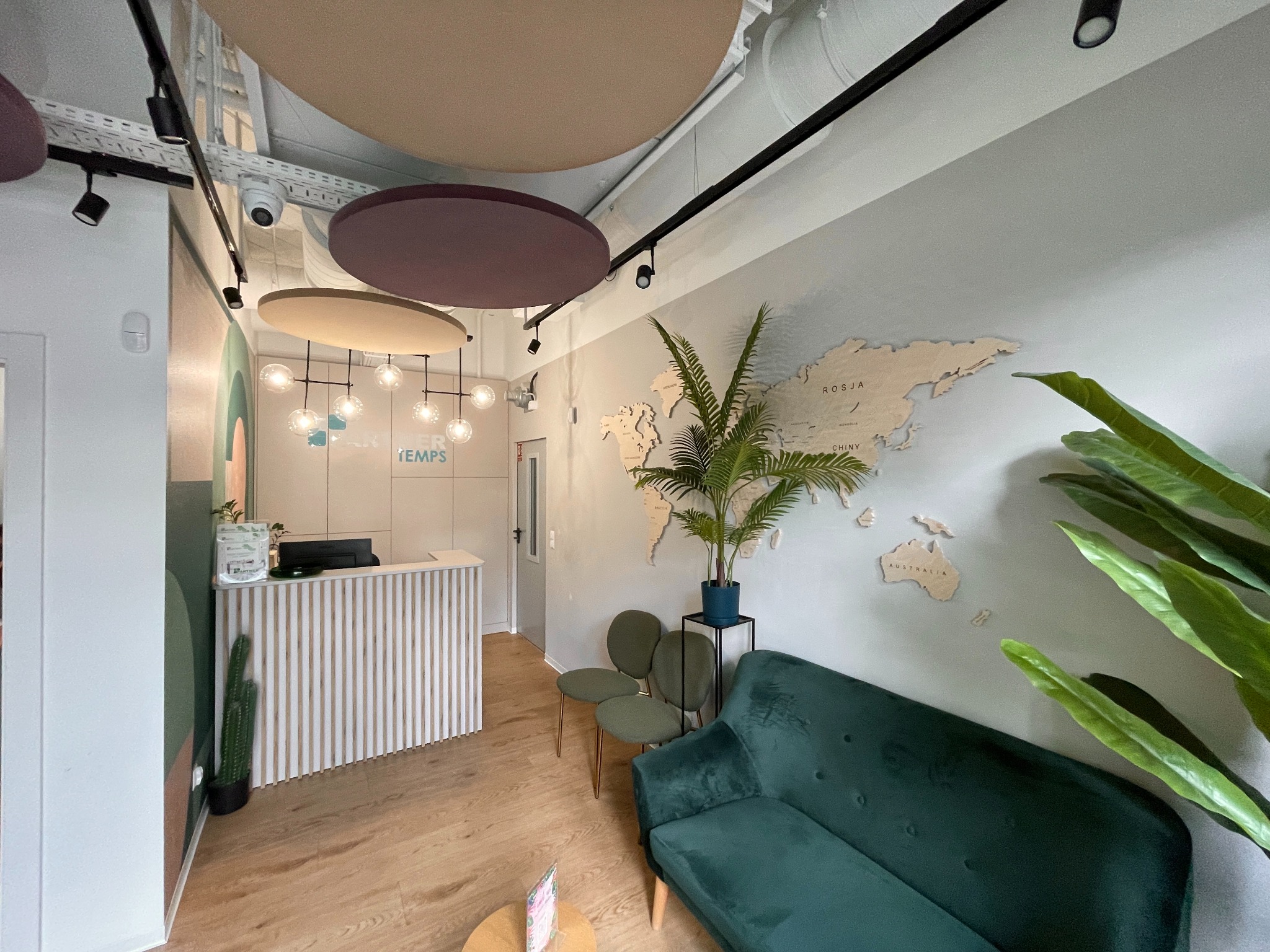 Nowoczesne biuro z recepcją, zieloną sofą i drewnianą mapą świata na ścianie, oświetlone designerskimi lampami.