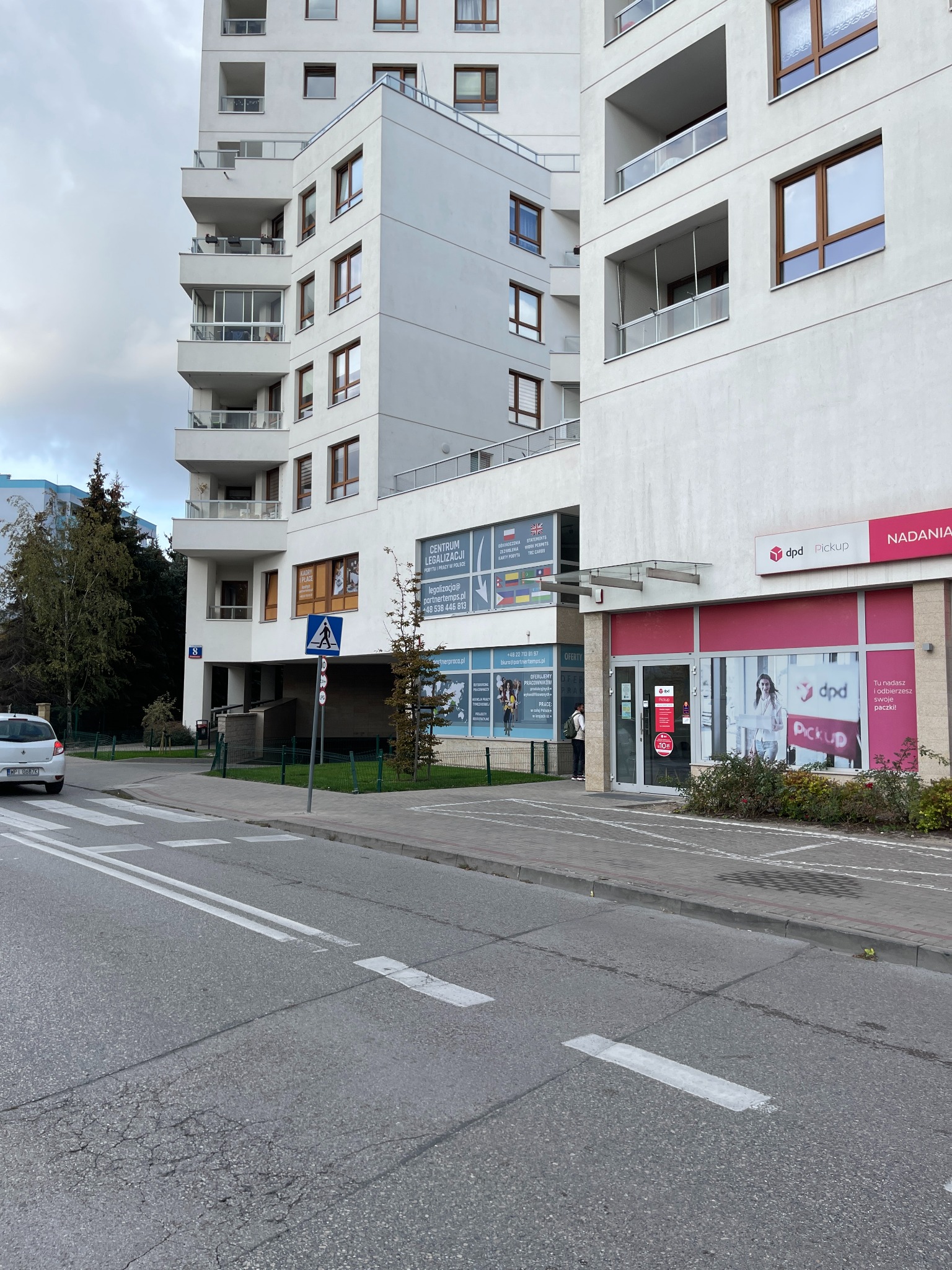 Budynek z biurami usług dla firm, w tym kadry i legalizacja pobytu, widoczny z ulicy z przejściem dla pieszych i zaparkowanym samochodem.
